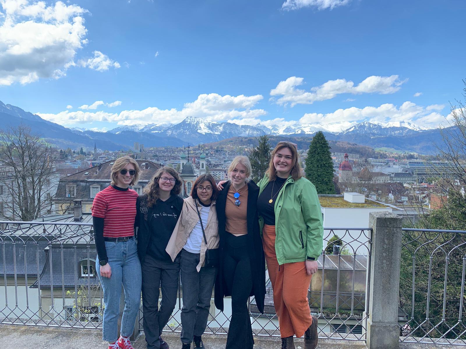 Students posing against a fence with mountains and a small city in the background